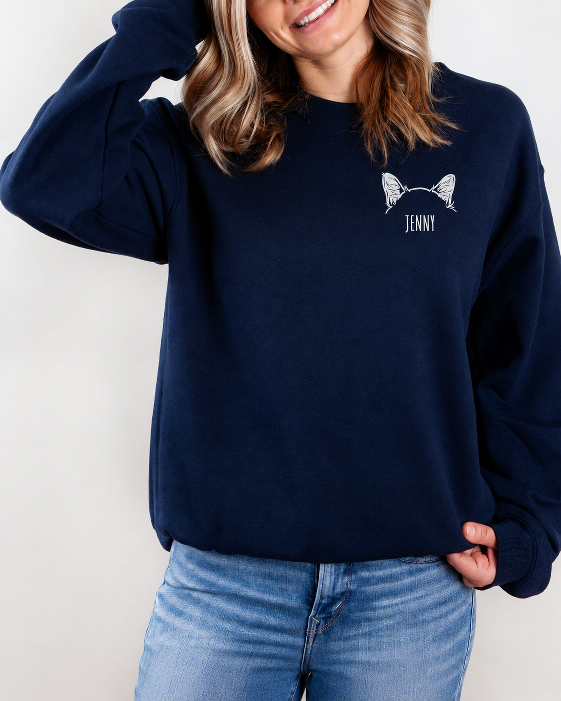 A woman wearing a navy blue crewneck sweatshirt with a white graphic of cat ears and the name 'JENNY' printed on the chest, paired with light blue jeans.