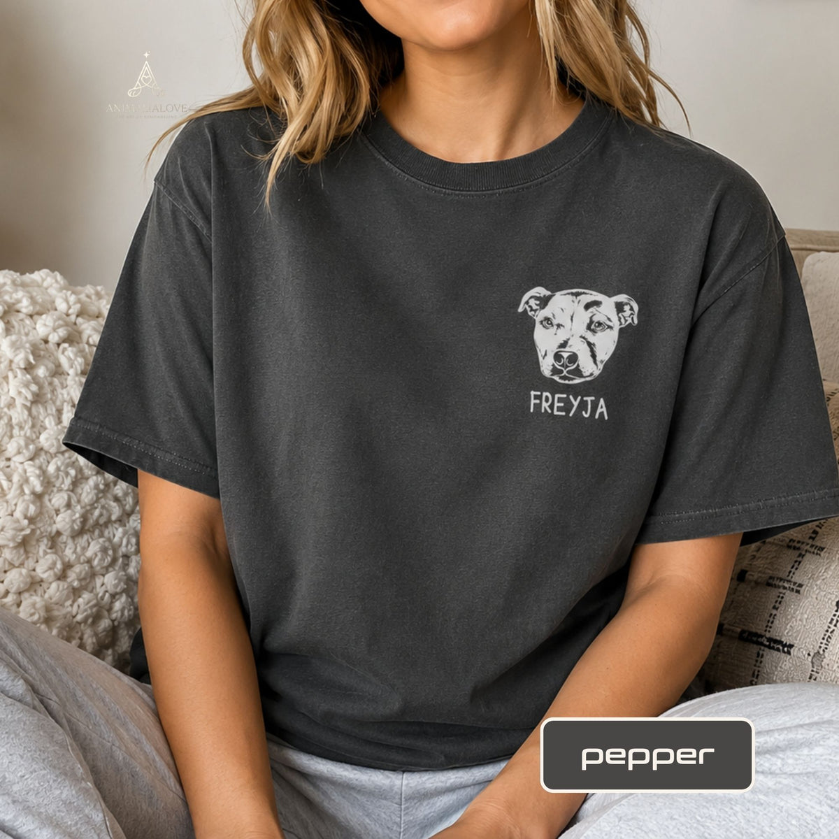 A woman wearing a dark charcoal gray t-shirt with a white graphic of a pitbull dog head and the text 'FREYJA' printed below it. A label at the bottom right reads 'pepper'.