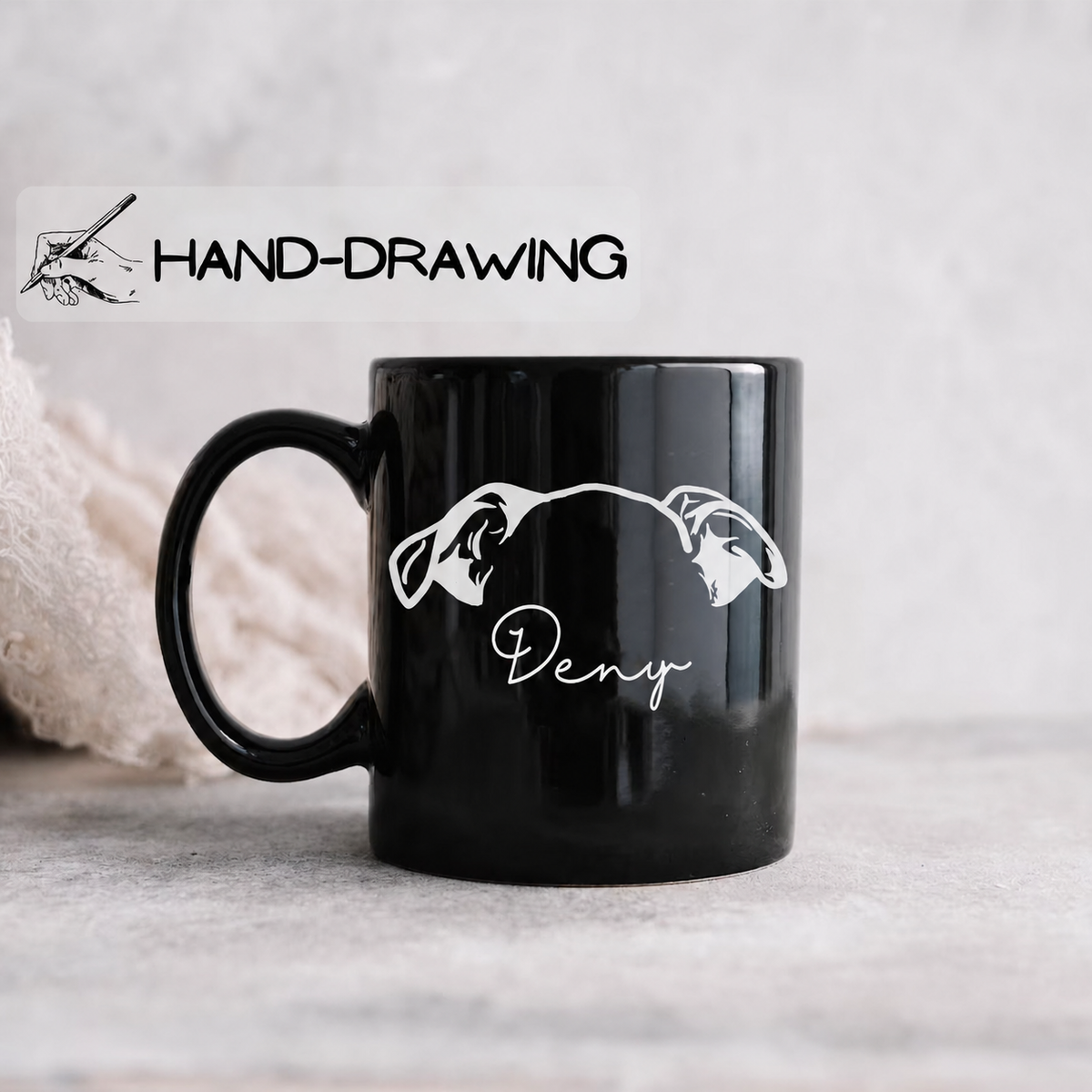 A glossy black ceramic mug with a white hand-drawn style graphic of two stylized dog heads and the word 'Deny' in script, shown on a light gray surface with a soft textured background. A white banner at the top reads 'HAND-DRAWING' with a small drawing icon.
