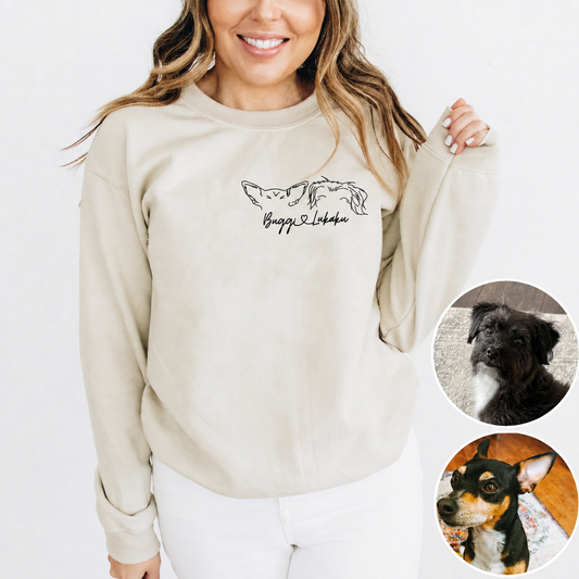 A woman wearing a light beige crewneck sweatshirt with a black line art graphic of two dogs and their name.