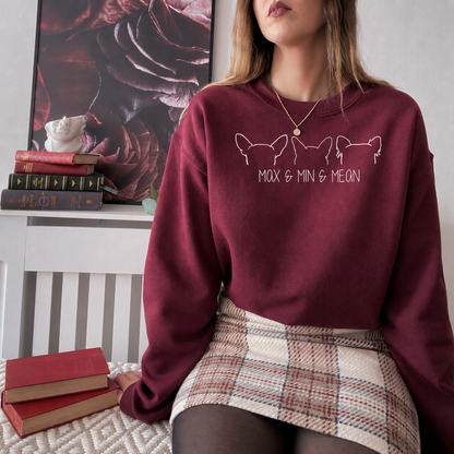 A woman wearing a maroon crewneck sweatshirt with white line art of three French bulldogs and the text 'MOX & MIN & MEON' on the front, paired with a plaid mini skirt.