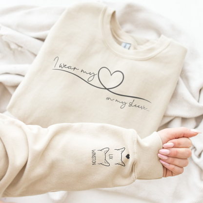 A beige crewneck sweatshirt with custom black graphic prints, shown styled with a hand wearing the matching long sleeve cuff.