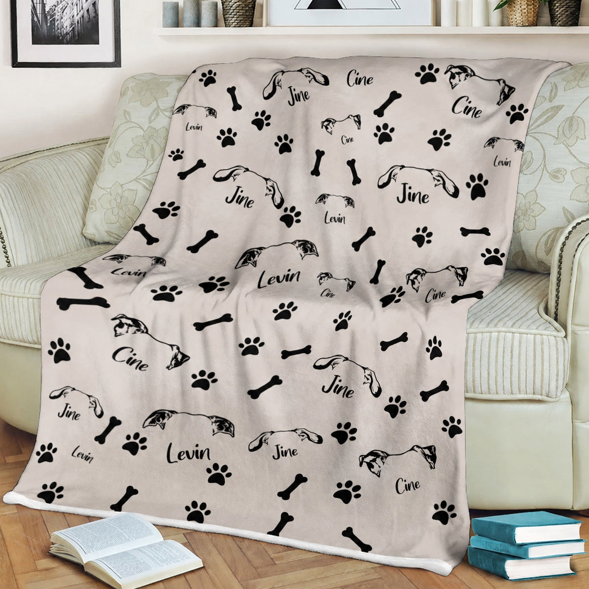 Cream personalized pet blanket displayed on a sofa with repeated pet ear illustrations, names, paw prints, and bones
