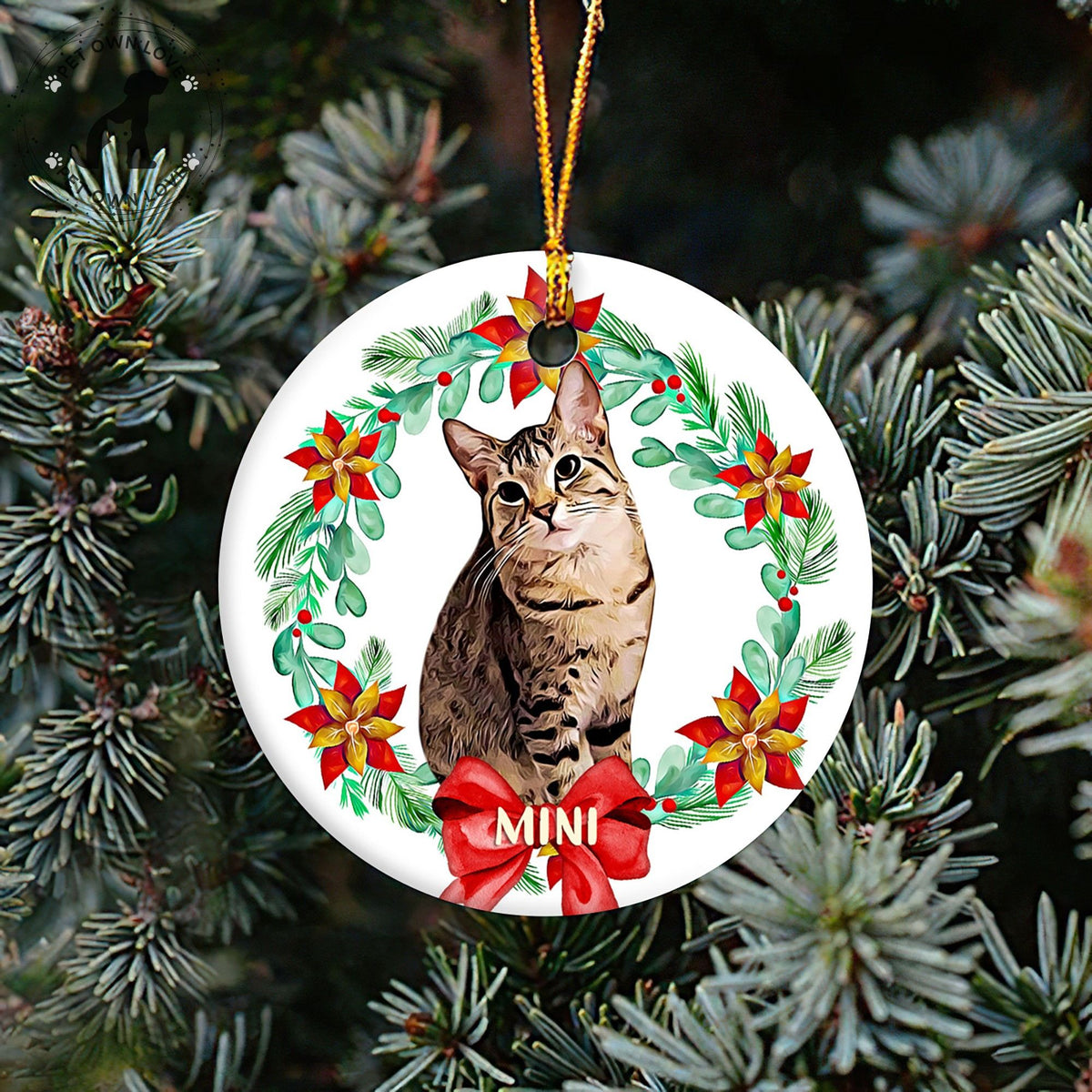 Personalized cat ornament hanging on a Christmas tree, featuring a tabby portrait, poinsettias, and a red bow