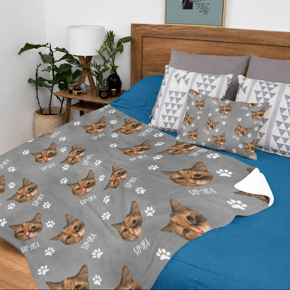 Personalized gray cat face blanket with repeated pet portraits, name text, and white paw prints on a bed