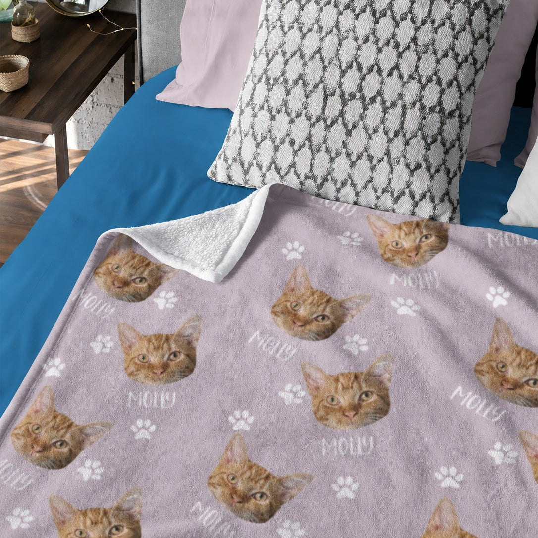 Pink custom cat face blanket with repeated orange tabby portraits, name text, and paw prints
