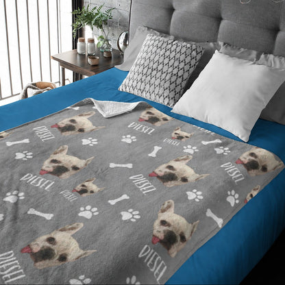 Gray personalized blanket with repeated small dog portraits, the name Dustin, paw prints, and bones on a bed