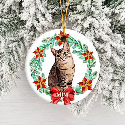 Personalized round ornament featuring a tabby cat in a floral wreath with a red bow and name